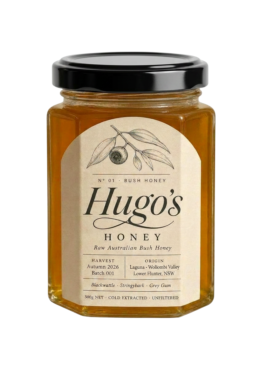 Amber glass jar of Hugo's Honey Raw Bush Honey with kraft label and shiny ridged lid, tilted against the farmhouse garden